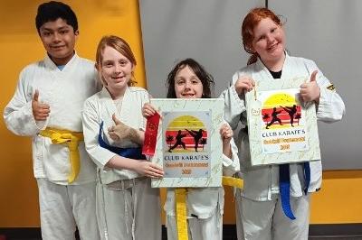 Standing pose of MMAA three girls and one boy, wearing kata, showing thumbs-up and holding awards.